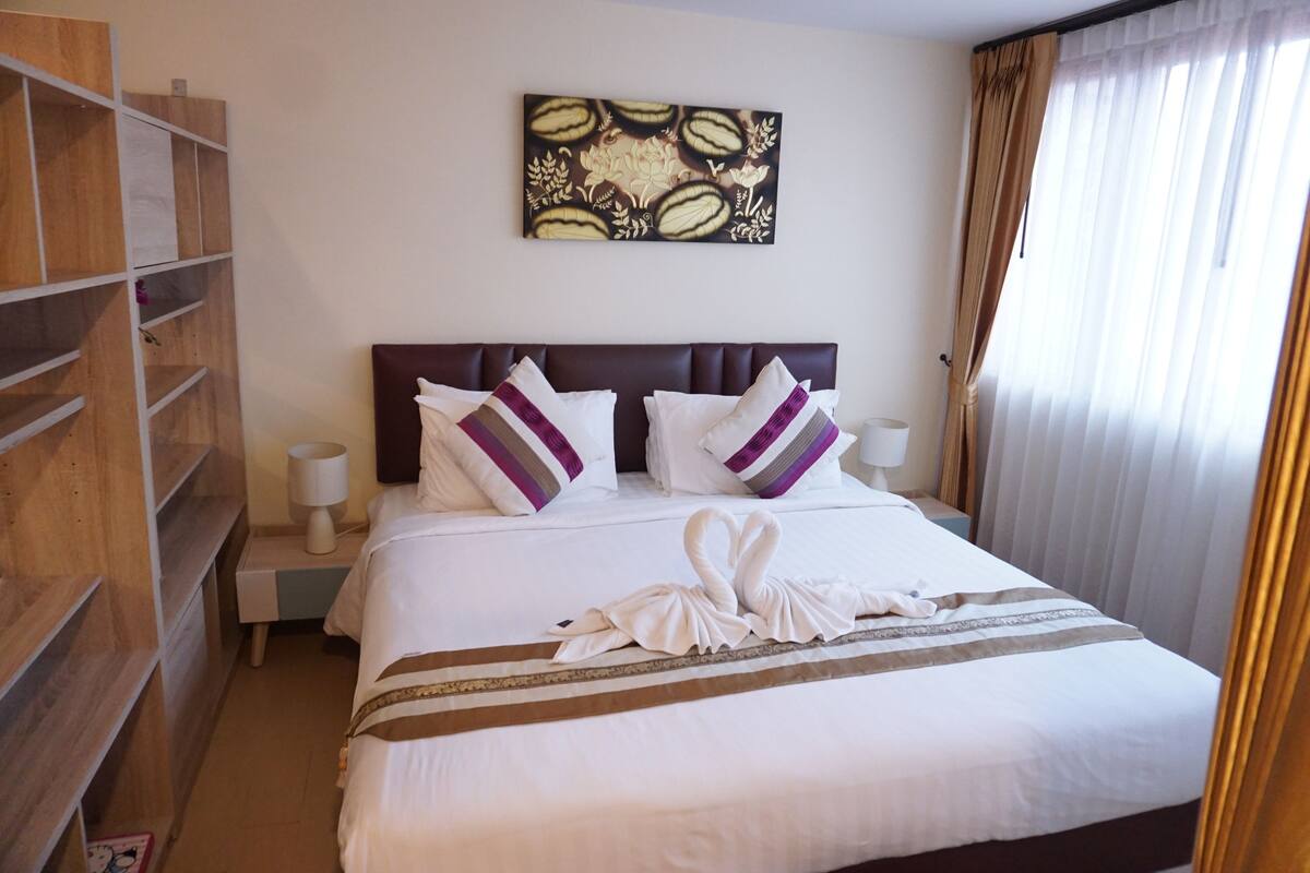 Une chambre d’hôtel avec un lit bien fait, une tête de lit, une œuvre d’art accrochée au mur et une fenêtre avec des rideaux.