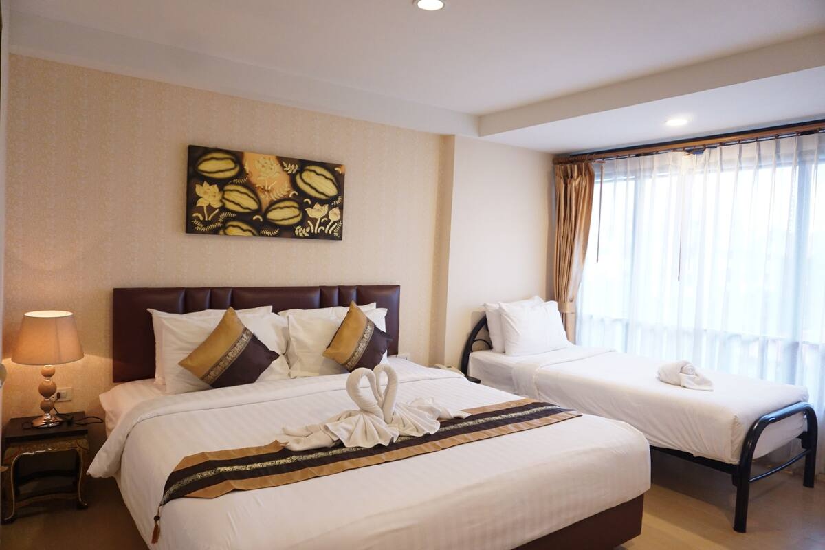 Une chambre d’hôtel avec deux lits, une tête de lit, une œuvre d’art murale, une fenêtre avec des rideaux et une table de chevet avec une lampe.