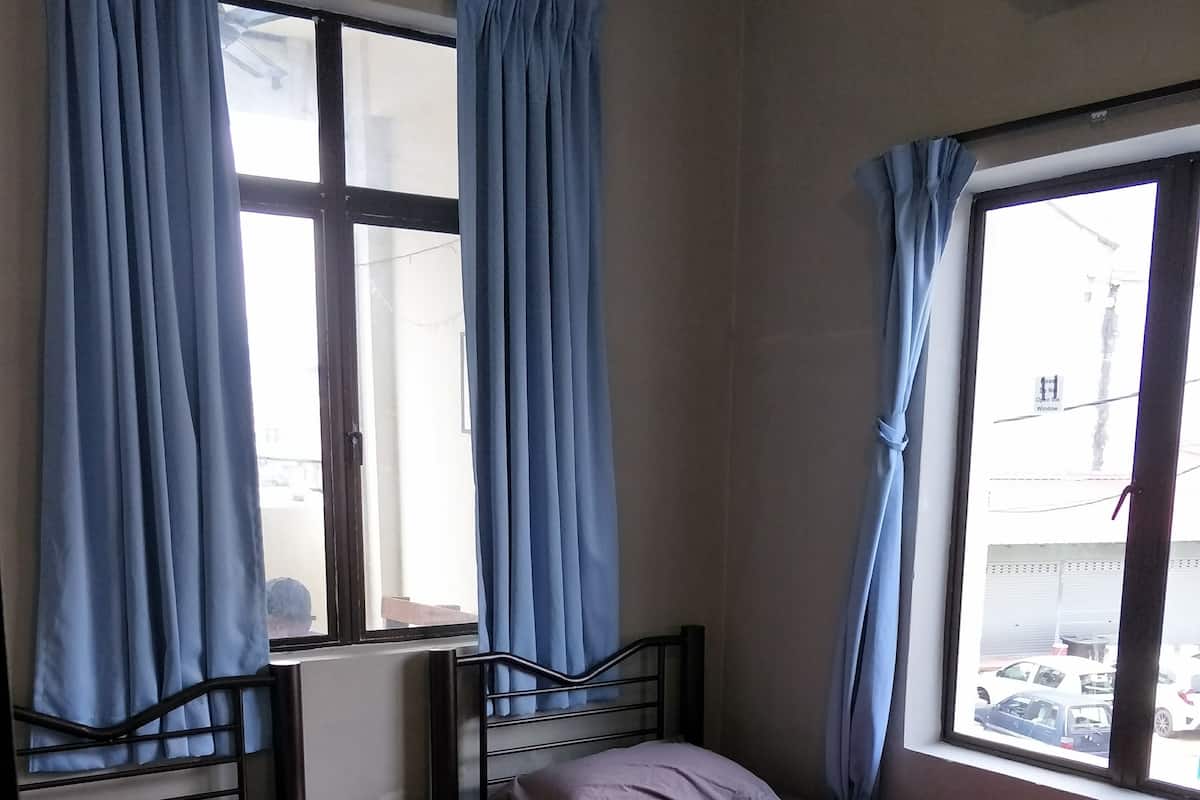 A small, simple room with two beds, a small table, and a window with curtains.