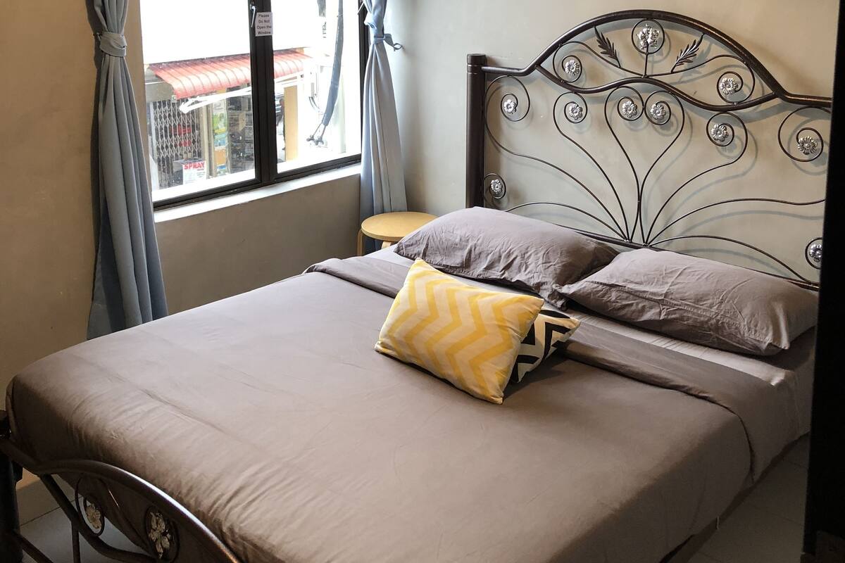 A bedroom with a metal bed frame, a window with curtains, a wall-mounted air conditioner, and a motivational quote sign.
