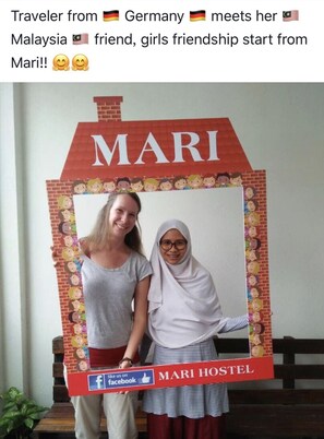 En fotobås med en husformad bakgrund dekorerad med texten ”MARI HOSTEL” och en Facebook-logotyp.