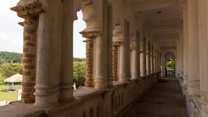 A corridor with columns and arches, leading to a covered area with a view of greenery. - Mari Hostel (Ipoh)