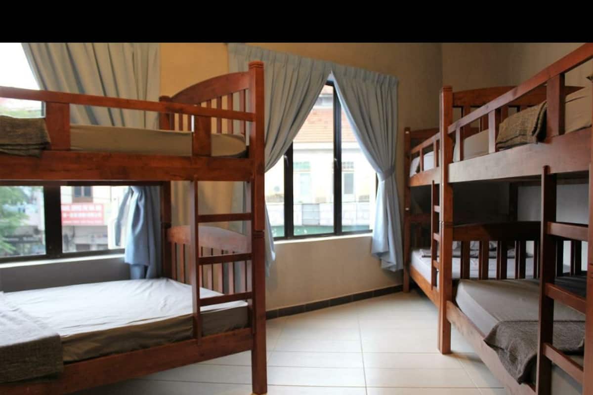 A dormitory room with bunk beds, a window with curtains, and a view of the outside.