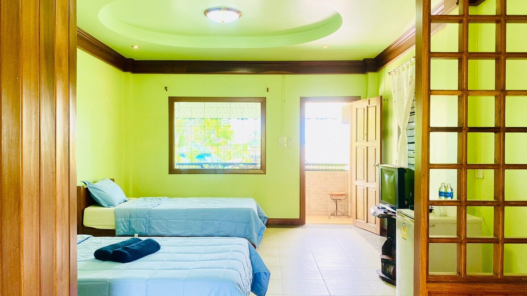 A room with two beds, a television, and a window with a view of greenery.