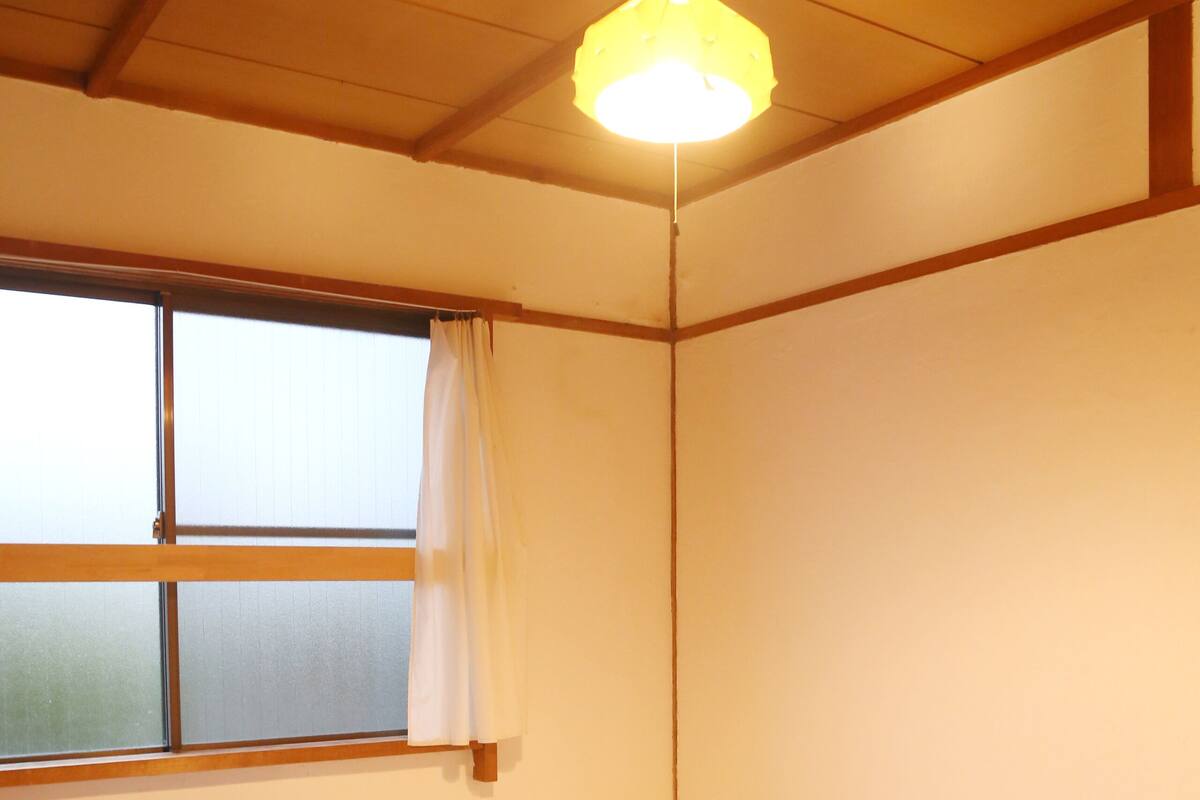 Ein Zimmer mit einem großen Bett, einem Vorhangfenster und einer hängenden Leuchte.