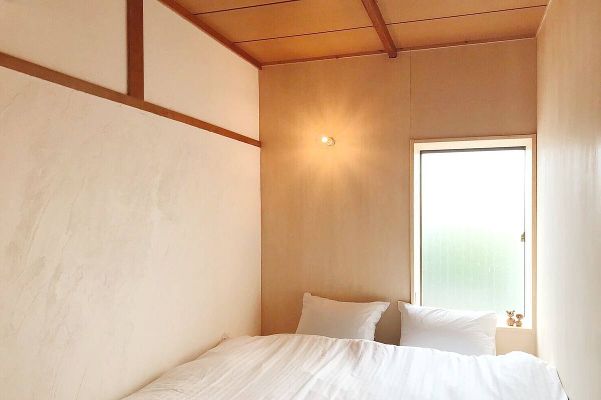 Ein Schlafzimmer mit einem Bett, Kissen, einem Fenster und einer wandmontierten Lampe.