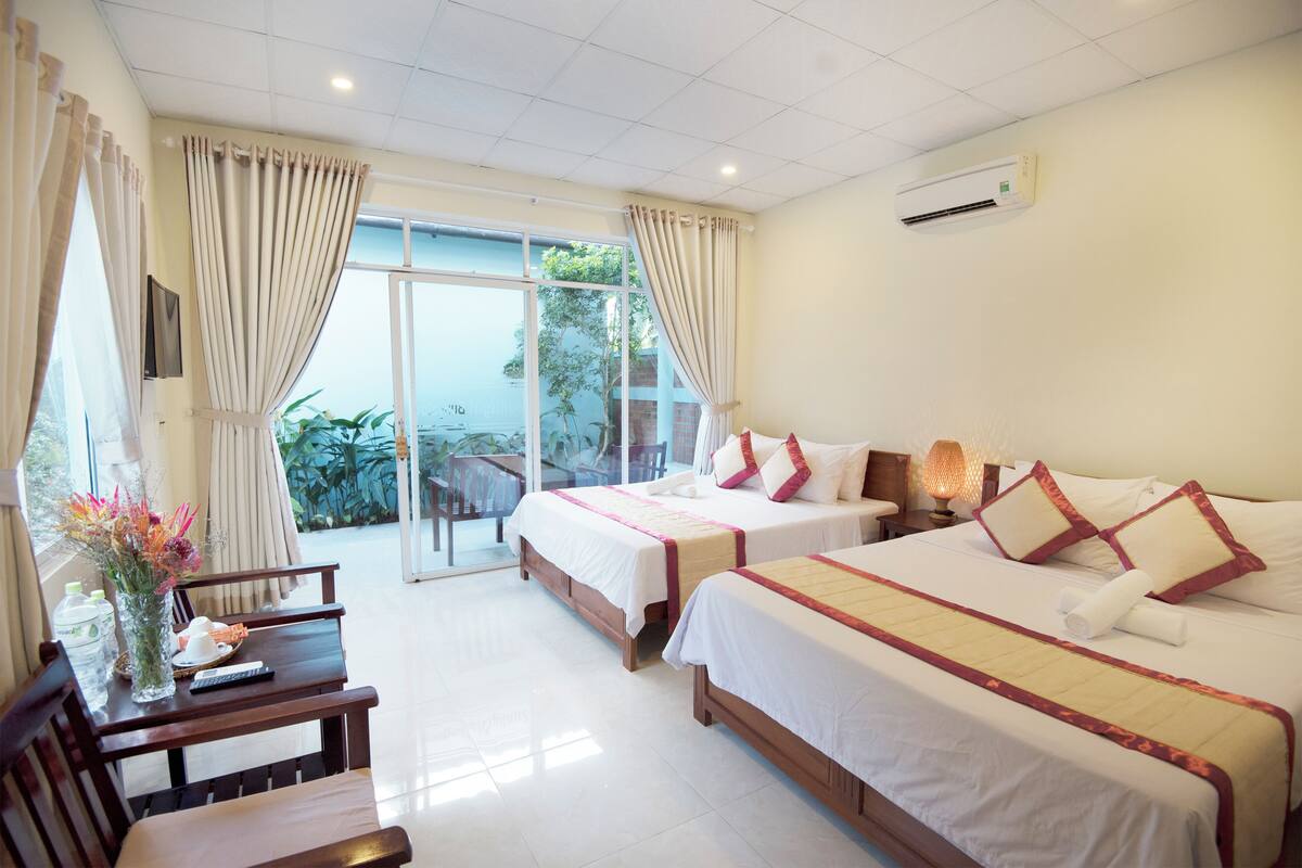 A hotel room with two beds, a desk with a chair, a TV, and a view of the outdoors.