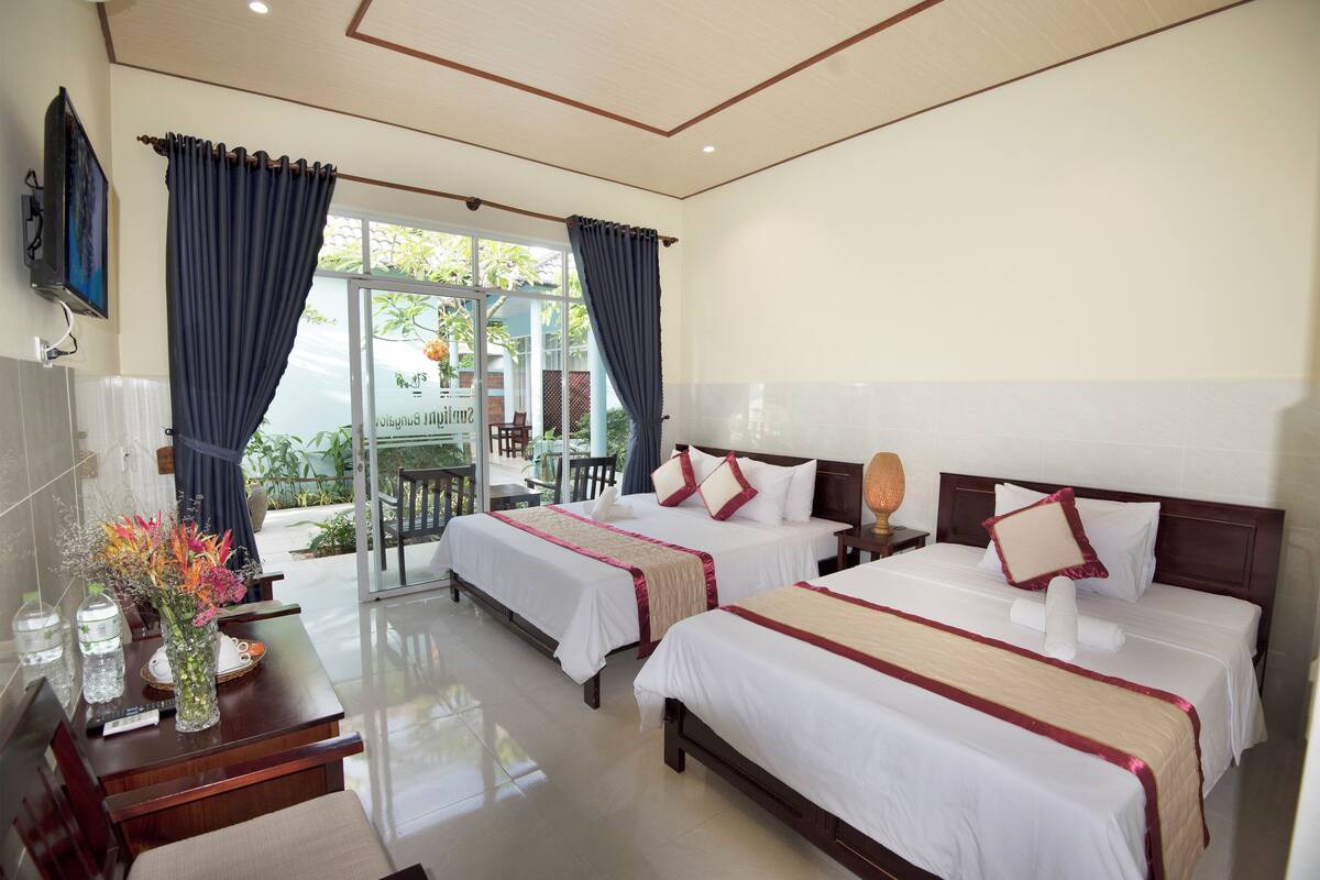 A hotel room with two beds, a desk, a TV, and a view of the outdoors.