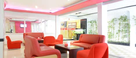 A modern lobby with red seating, a reception desk, and a digital screen.