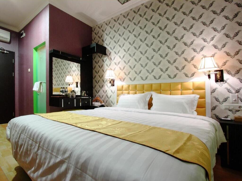 A hotel room with a large bed, a green door, a mirror, and patterned wallpaper.