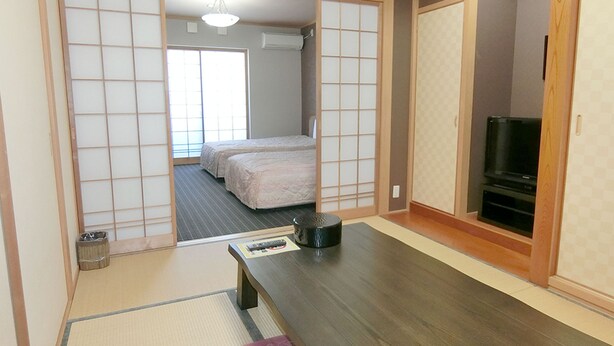 Una habitación japonesa tradicional con suelo de tatami, futón, televisor y puertas correderas.