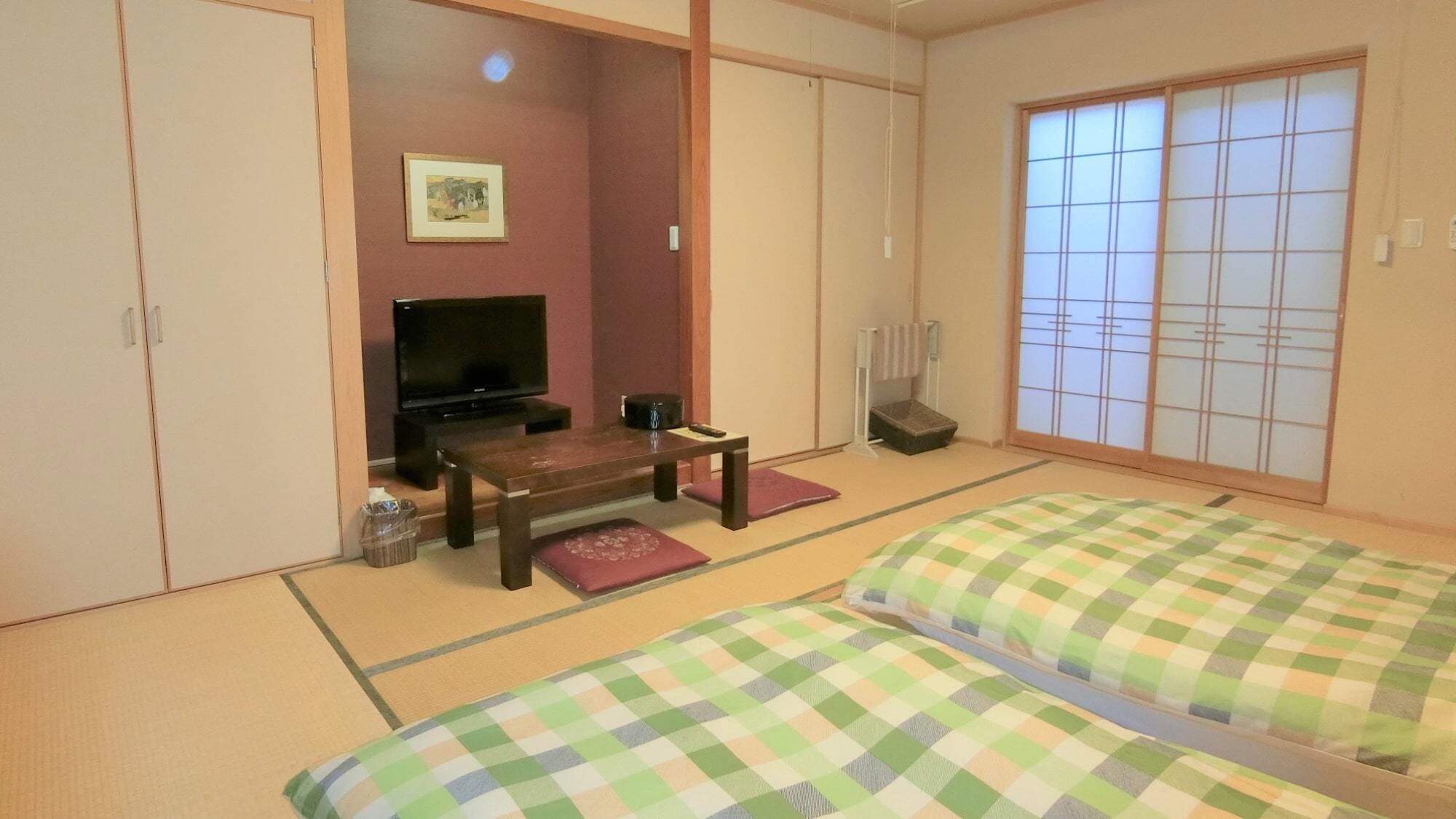 A traditional Japanese room with tatami flooring, a television, a small table, and futon beds.