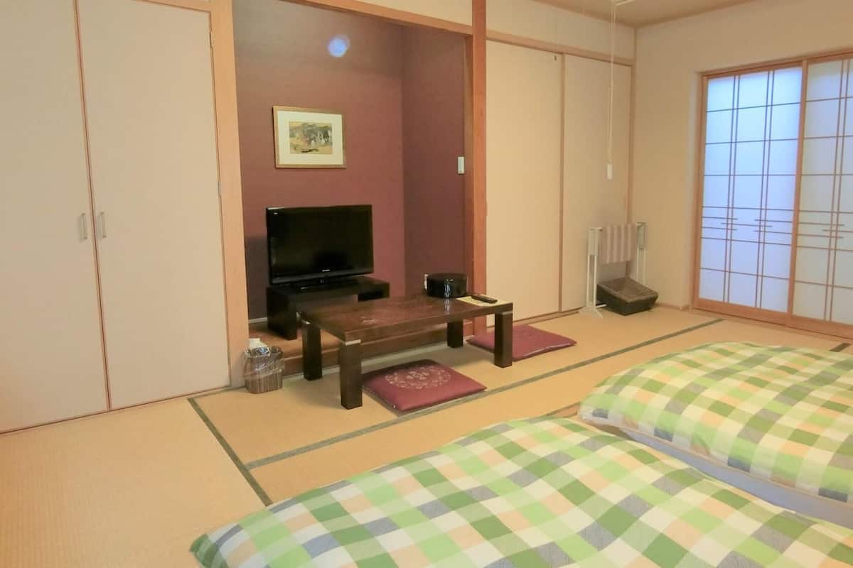 Een traditionele Japanse kamer met tatami vloerbedekking, een televisie, een klein tafeltje en futonbedden.