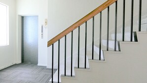 Una escalera con barandilla de madera y balaustres negros, que conduce a un rellano con una puerta.