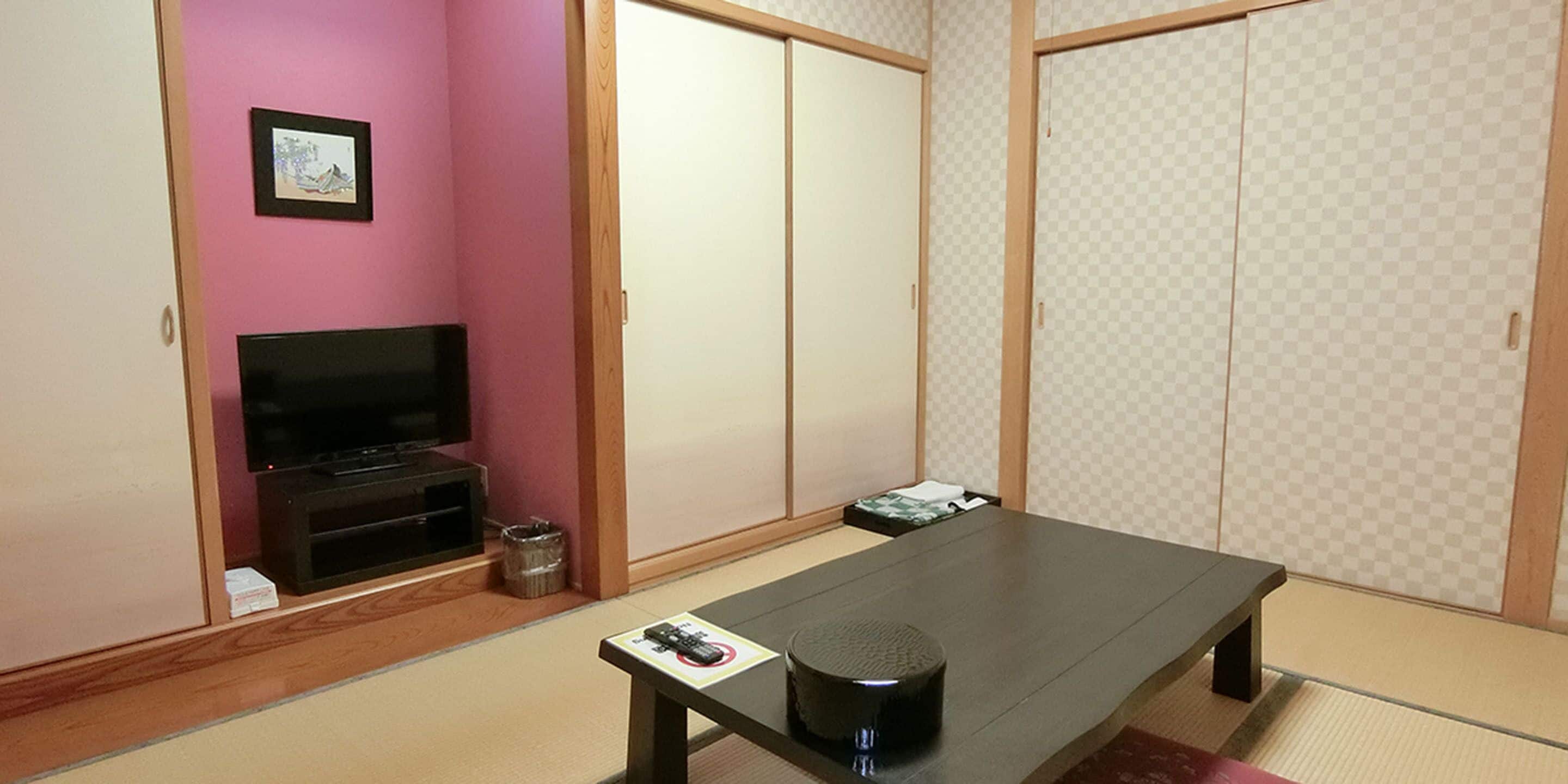 A room with a television, a tatami mat, a low table, and sliding doors.