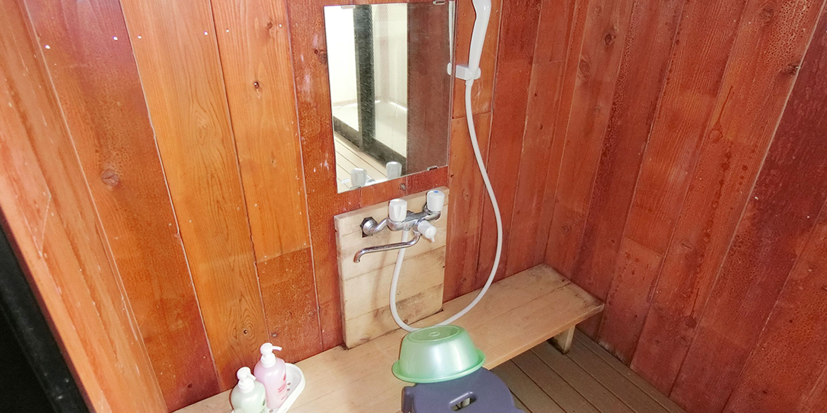 Baño de cabaña de madera con banca de madera, espejo, lavabo y dos dispensadores de jabón.