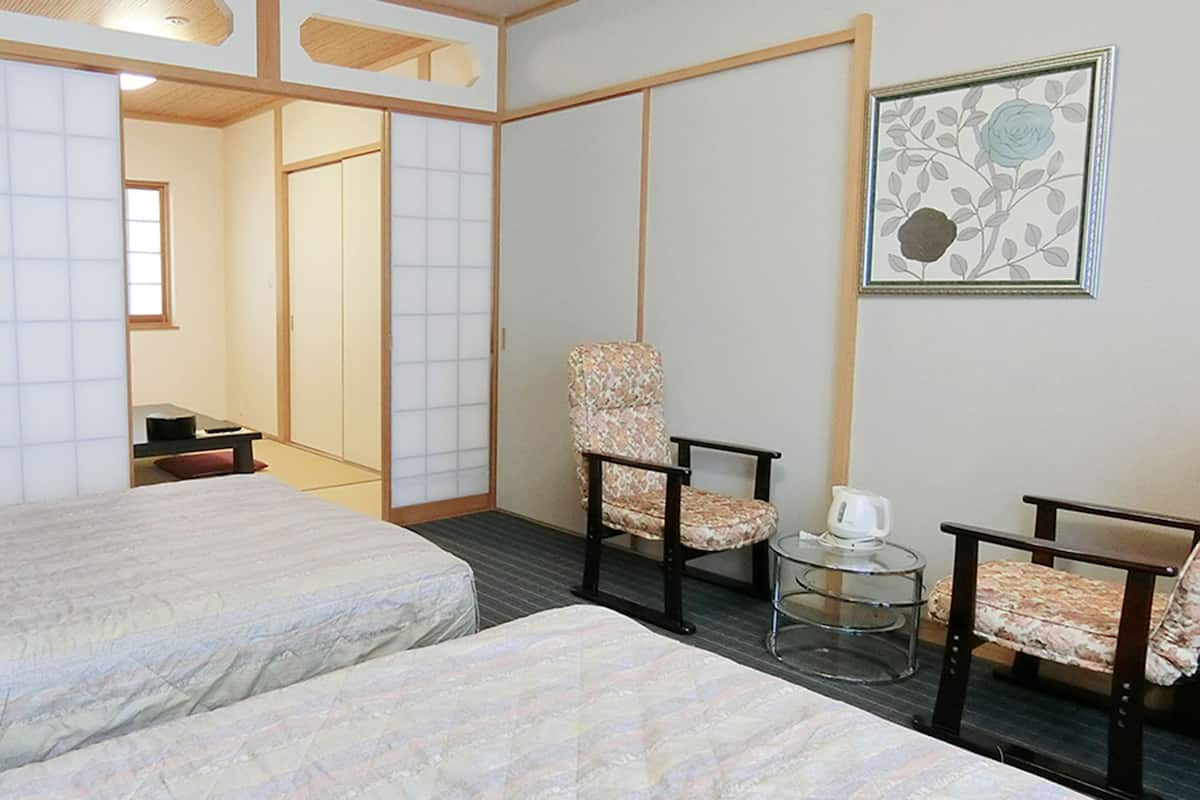 A hotel room with two beds, a chair, a small table, and a picture on the wall.