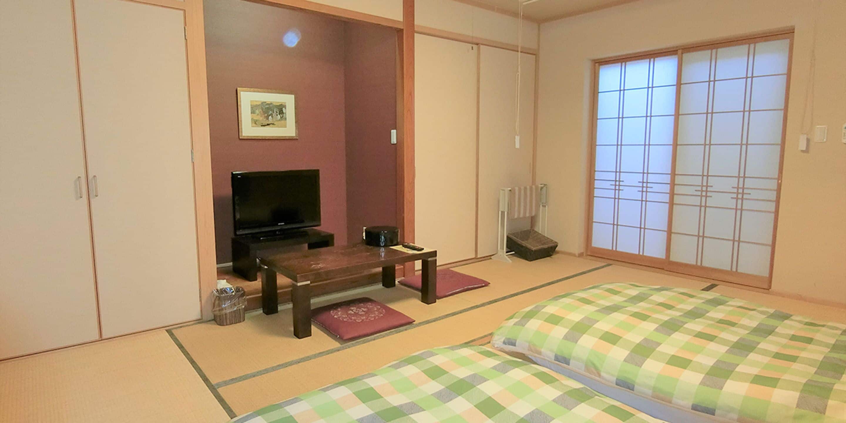 Una habitación japonesa tradicional con suelo de tatami, televisor, una mesita pequeña y camas futón.