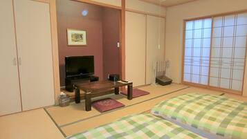 Una habitación japonesa tradicional con suelo de tatami, televisor, una mesita pequeña y camas futón.