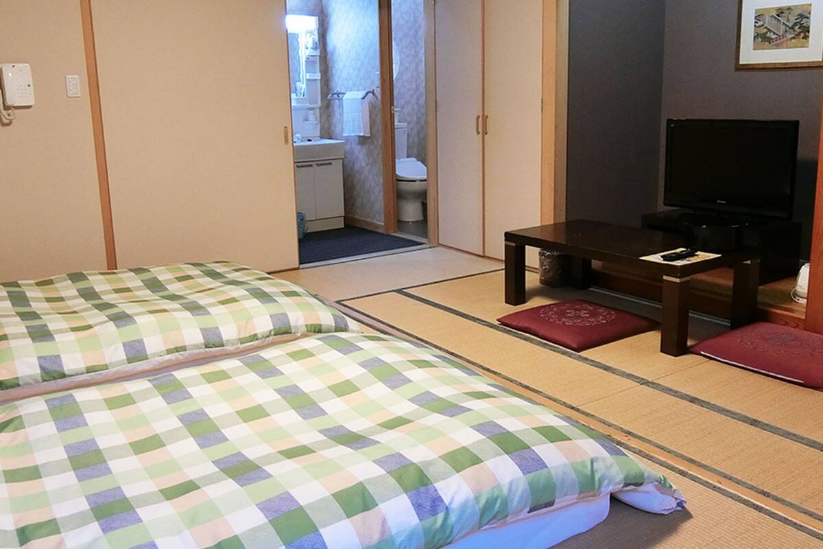 A room with two beds, a small table, a television, and a bathroom visible through an open door.