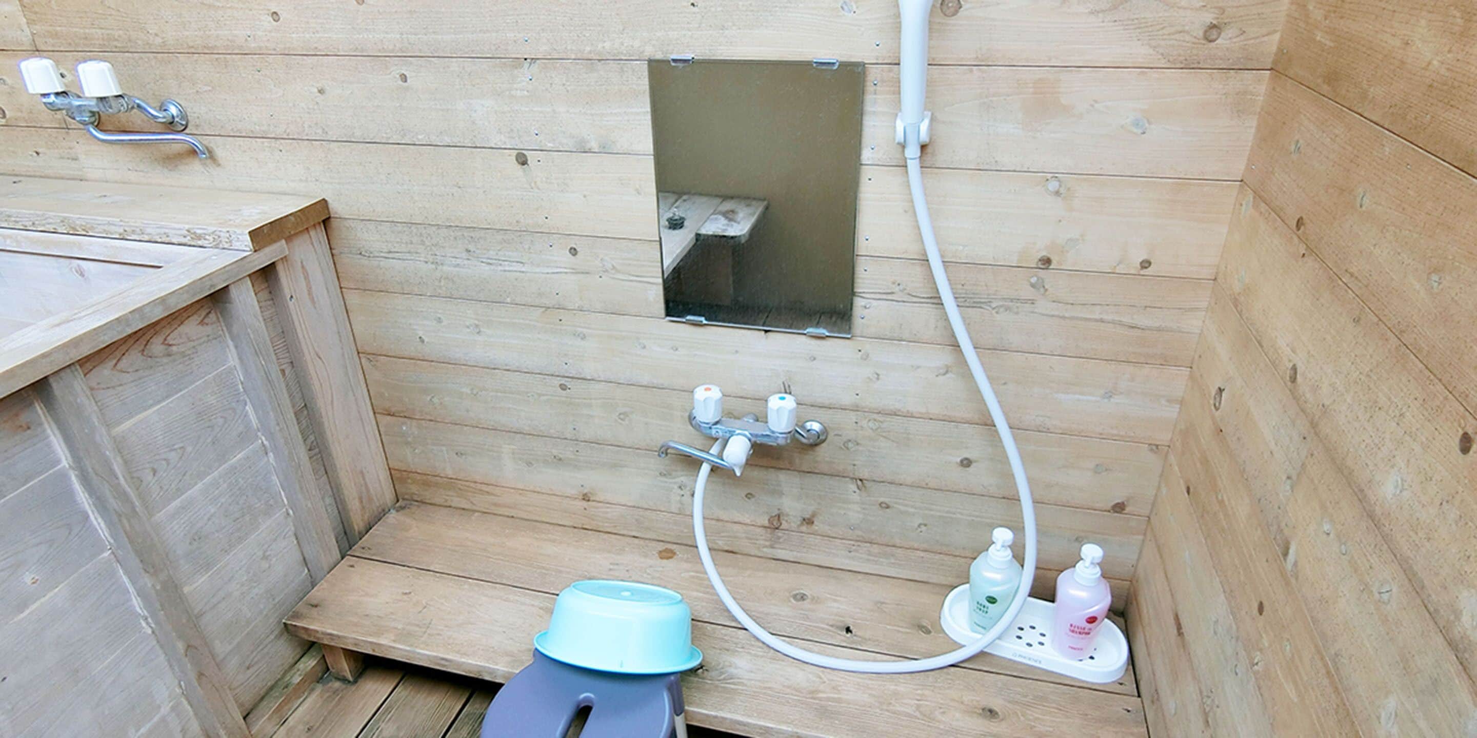 A wooden sauna with a bench, a small window, and a shower area with a hose and soap dispensers.