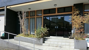 Un edificio moderno con una amplia entrada de vidrio, una escalera que conduce a la entrada y un letrero con caracteres japoneses.