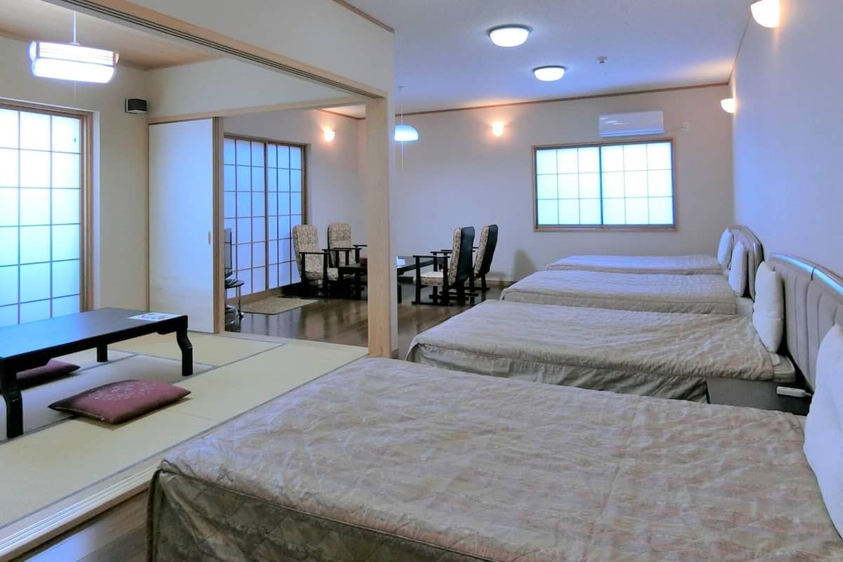 A hotel room with three beds, a small table, chairs, and a sliding door leading to a dining area.