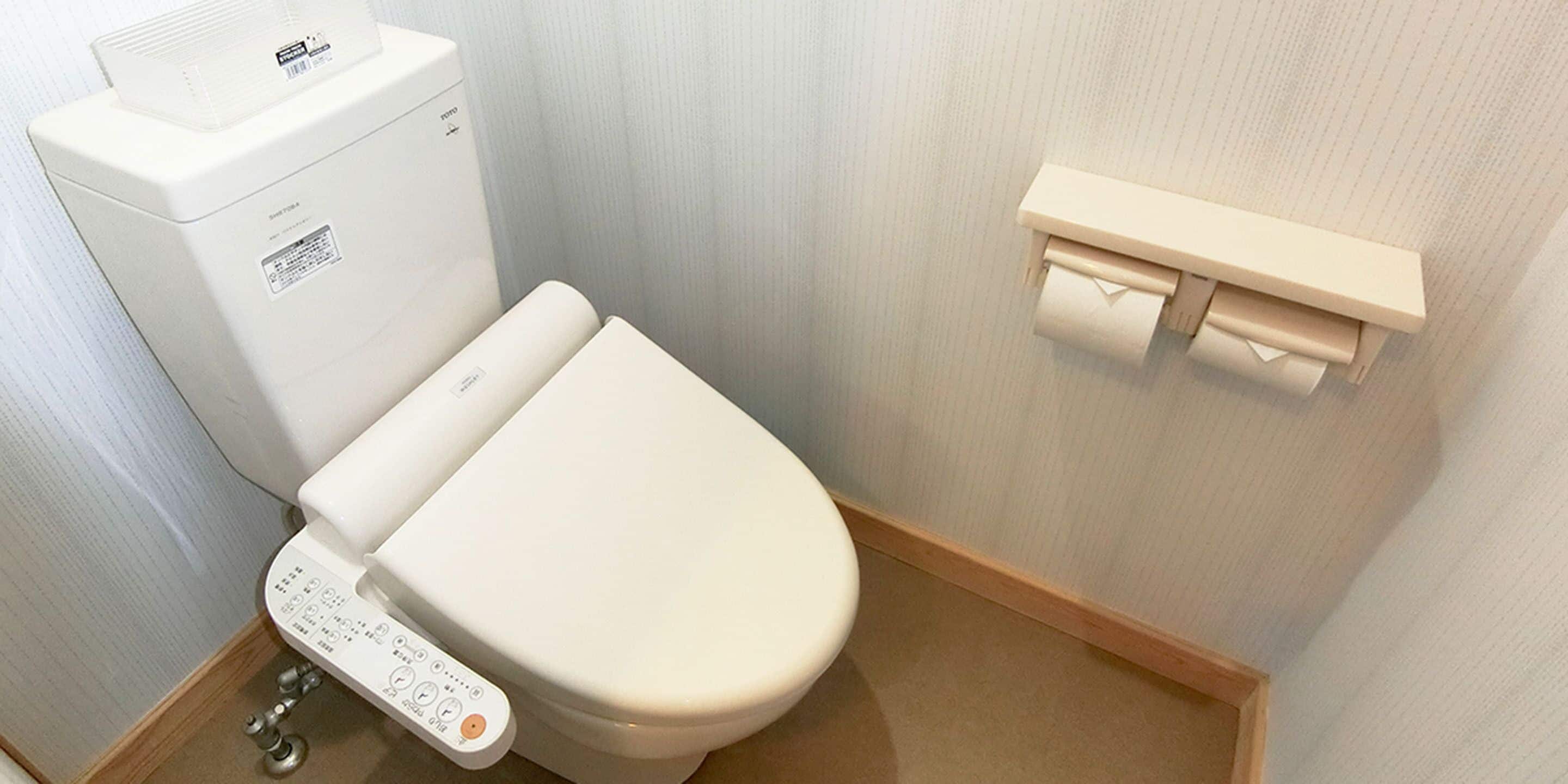 A modern toilet with a control panel, a toilet paper holder on the wall, and a white toilet tank.