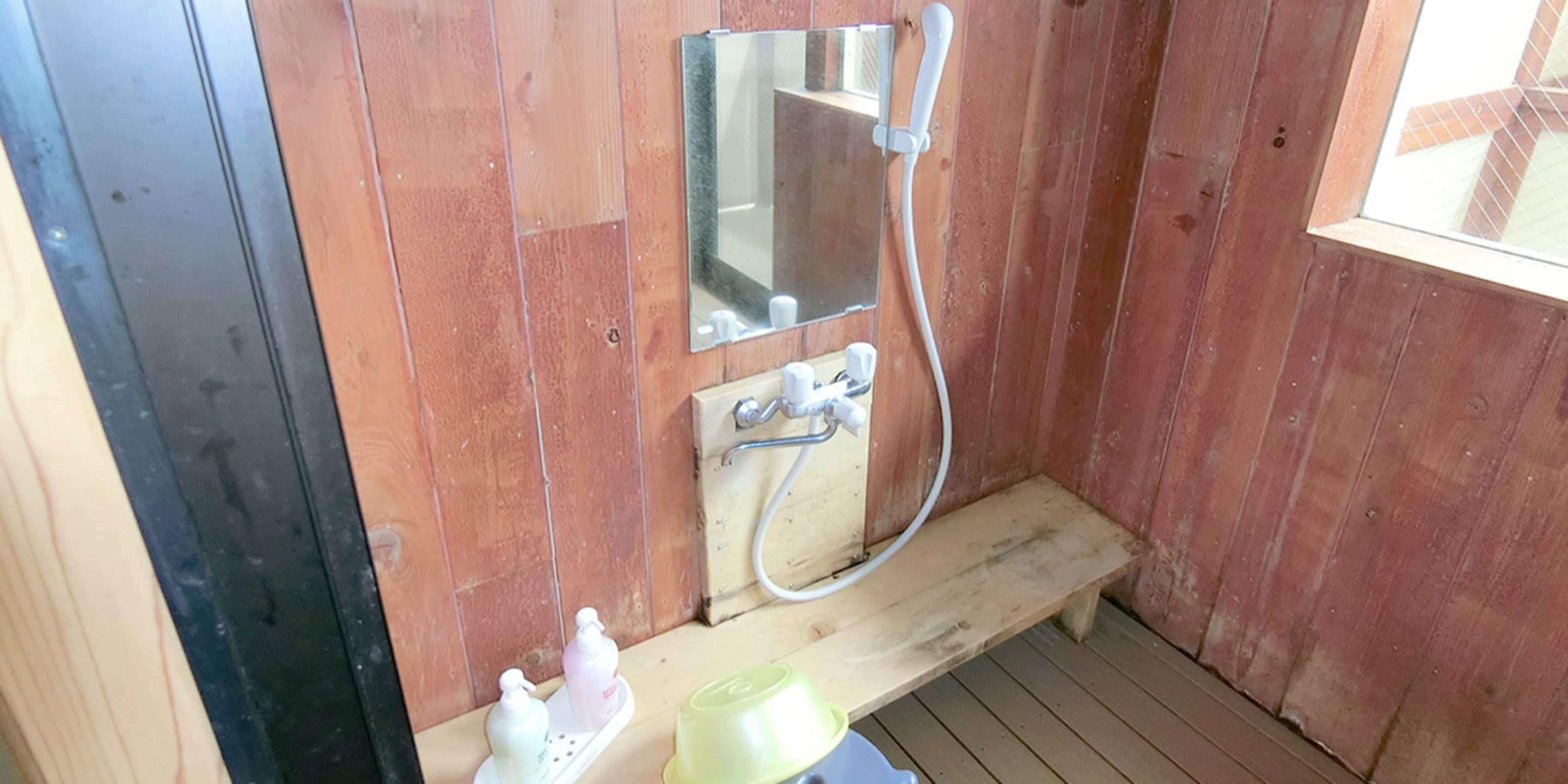 Baño de cabaña de madera con banca de madera, espejo, ducha y artículos de aseo sobre la banca.