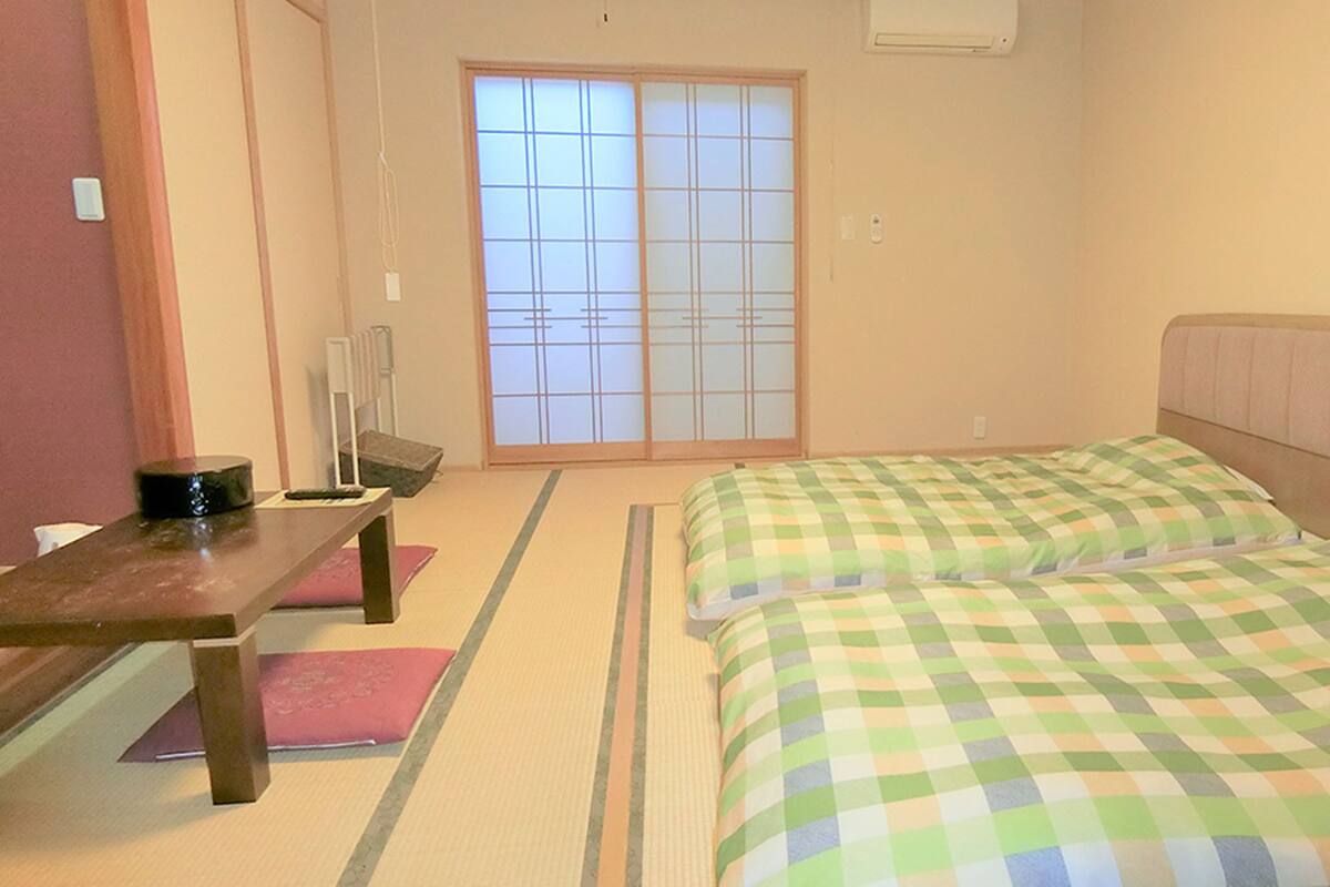A room with tatami mats, a futon bed, a wooden table, and a sliding door.