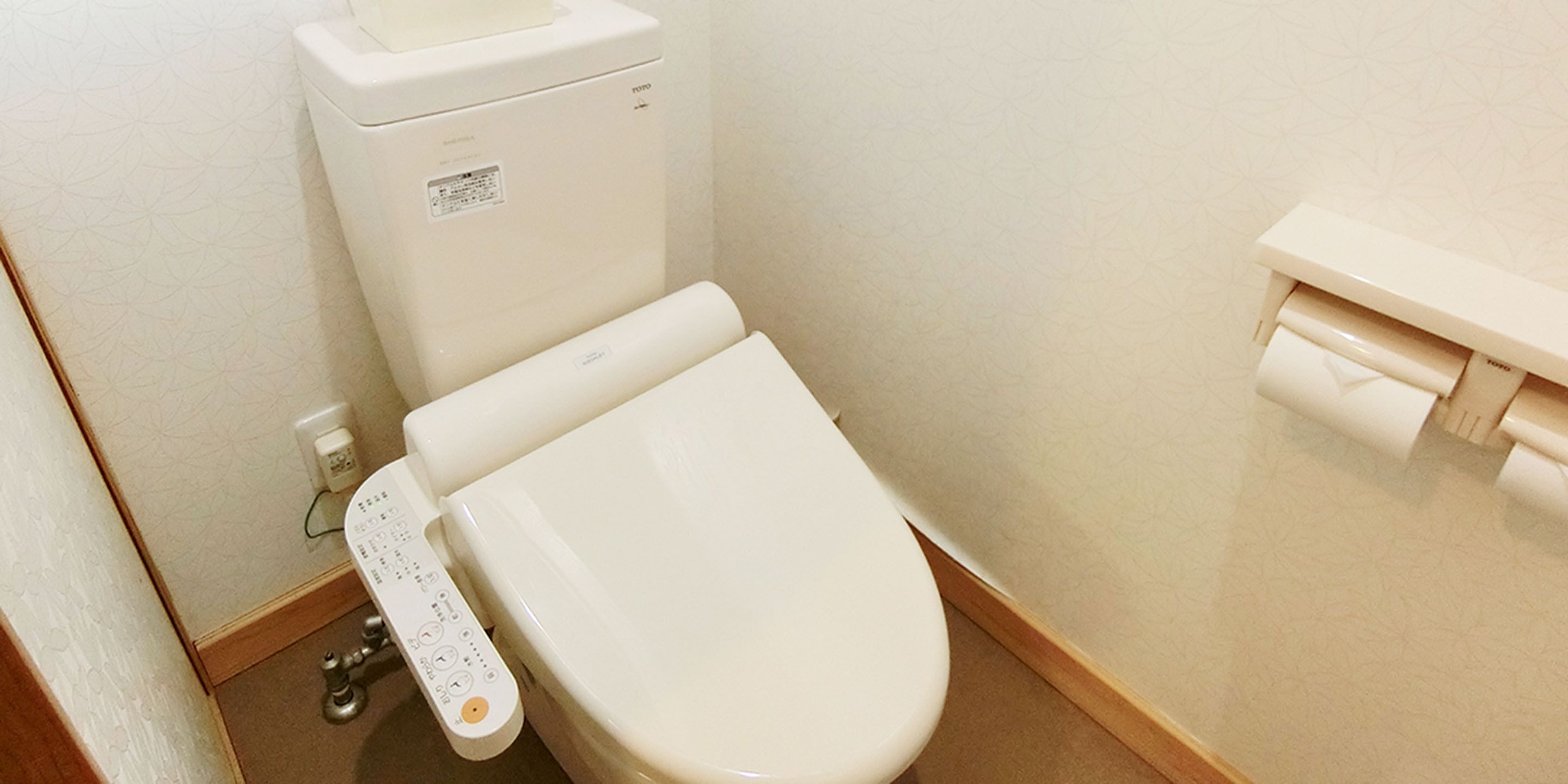 A modern toilet with a control panel, a toilet paper holder, and a wall-mounted flush button.