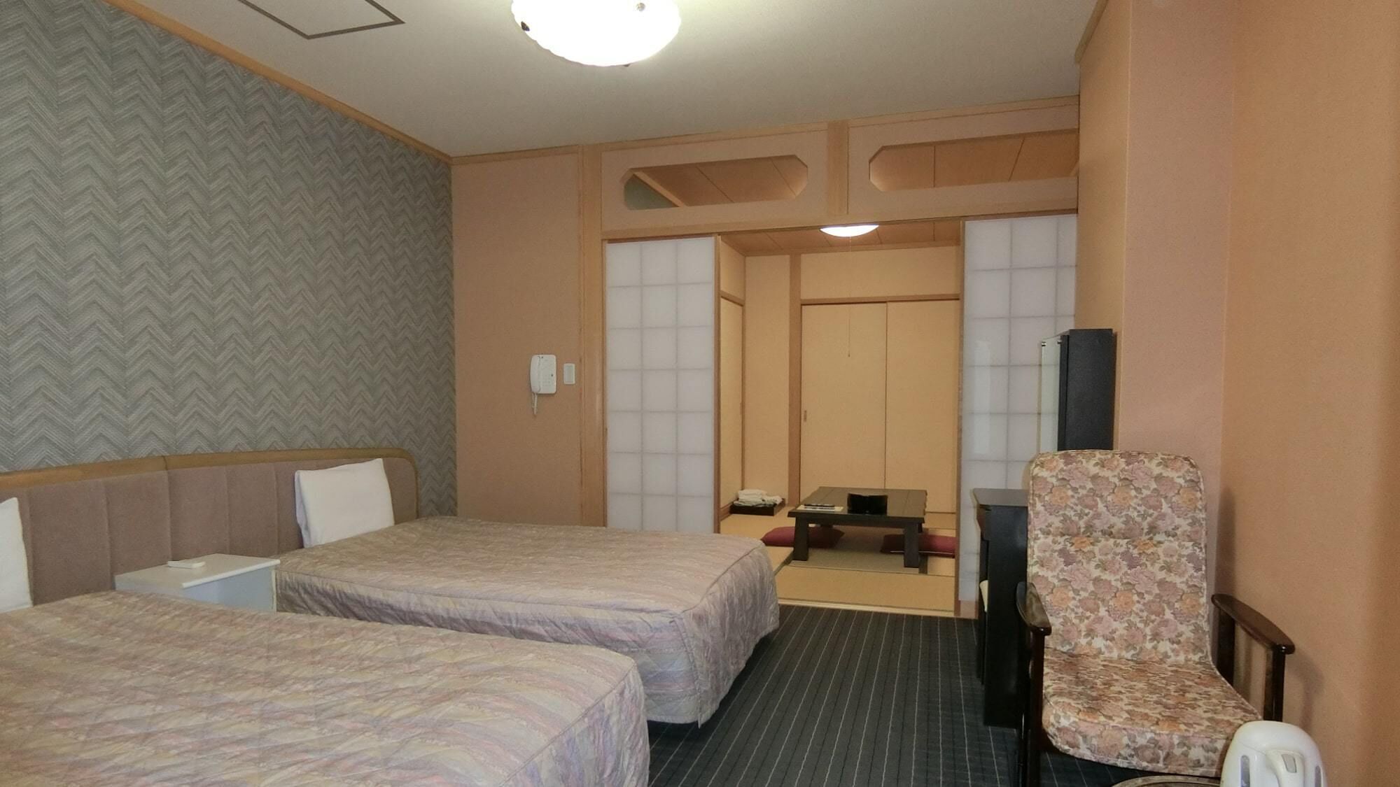 A hotel room with two beds, a desk, a chair, and a television.