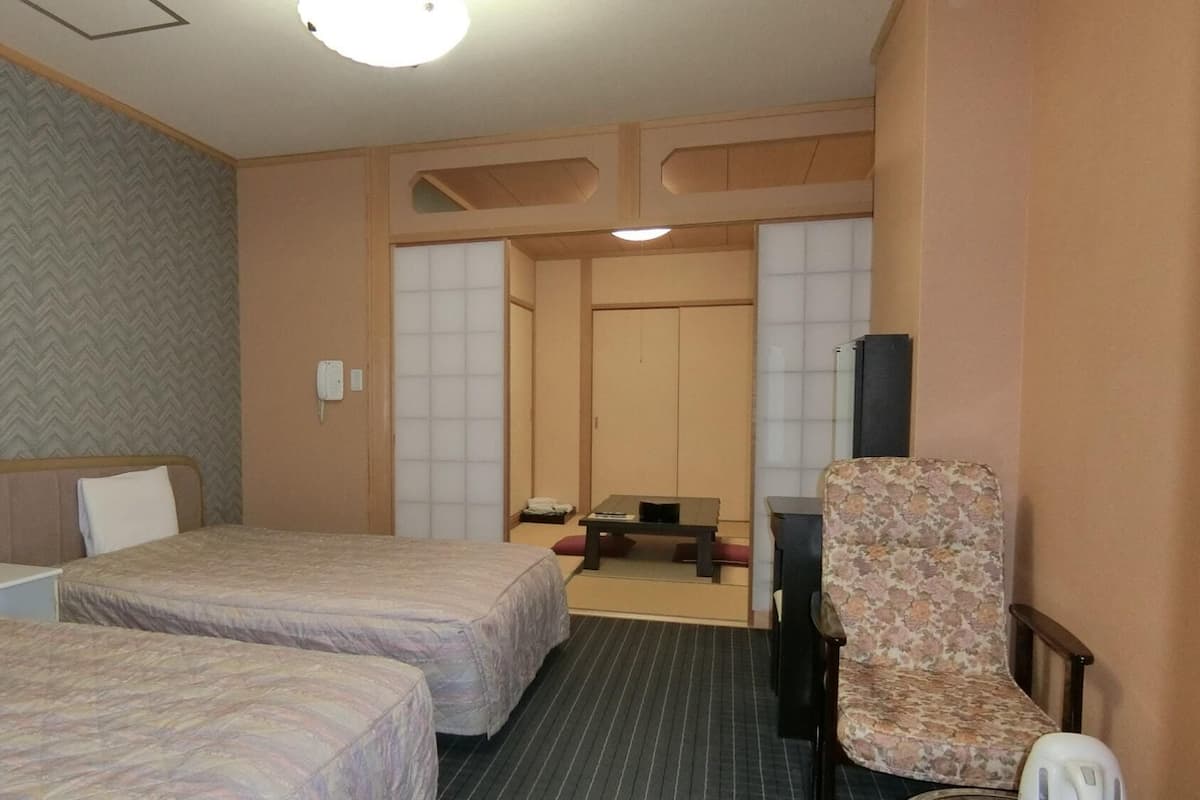 A hotel room with two beds, a desk, a chair, and a television.