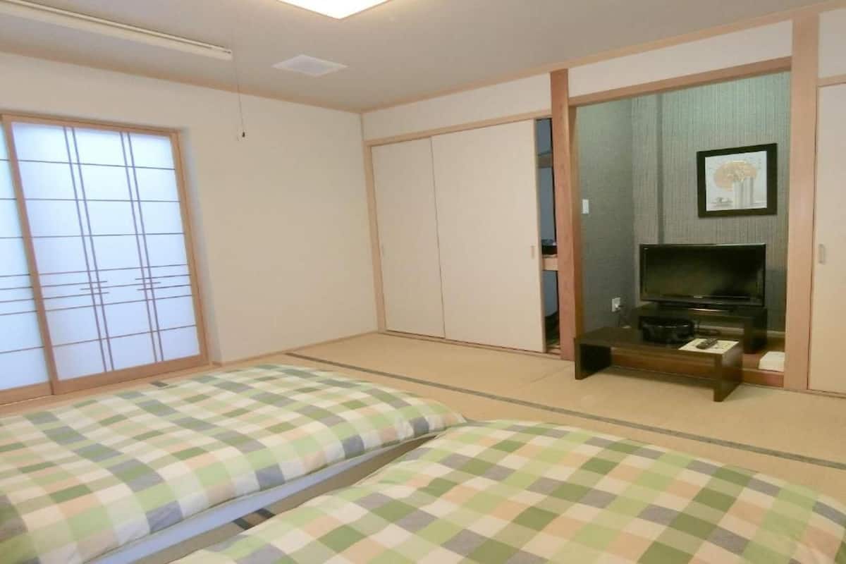 Een kamer met tatami vloerbedekking, een televisie en een schuifdeur.