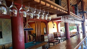 Zona bar con tavolo da biliardo, arredi in legno e lampade a sospensione.