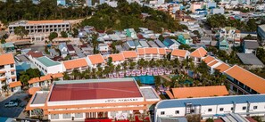 A large building with a red roof and multiple balconies, surrounded by smaller buildings and palm trees. - Aquaki Resort & Spa (Ha Tien)
