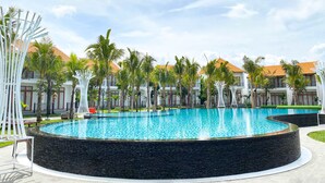 Ein Resort mit großem, kreisförmigen Pool, Palmen und einem Gebäude mit Ziegeldach.