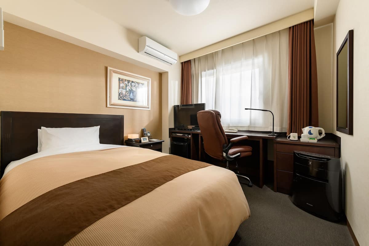 Hotelkamer met een groot bed, een bureau met stoel, een televisie en een airconditioner.
