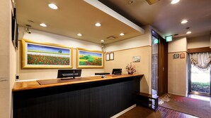A reception desk with two framed paintings, a black desk phone, and a small vase with flowers. - Hotel Sealuck Pal Kofu (Kofu)