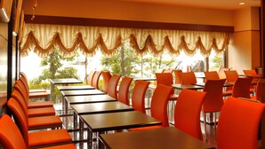 A conference room with rows of tables and orange chairs, large windows with curtains, and recessed ceiling lighting. - Hotel Sealuck Pal Kofu (Kofu)