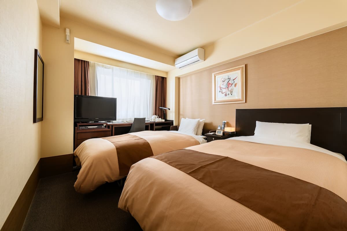Een hotelkamer met twee bedden, een bureau met een computer, een televisietoestel en een raam met gordijnen.