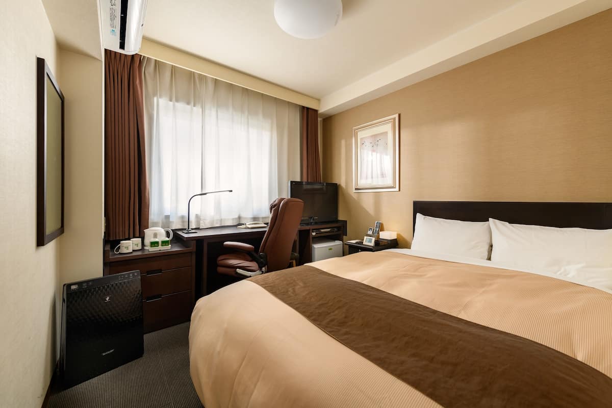 Hotelkamer met een bed, een bureau met een computer, een stoel, een televisie en een klein tafeltje met een kopje en een boek.