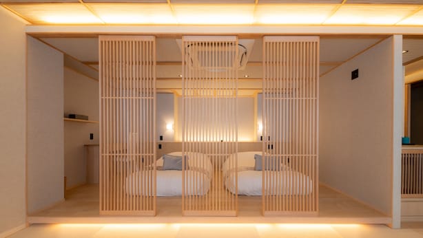 A modern hotel room with two beds separated by a wooden partition, a ceiling fan, and a small table with a lamp. - Hotel ISAGO Kobe (Kobe)