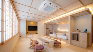 A modern, well-lit room with a wooden ceiling, a flat-screen TV mounted on the wall, a sofa set, and a small dining area with a table and chairs. - Hotel ISAGO Kobe (Kobe)