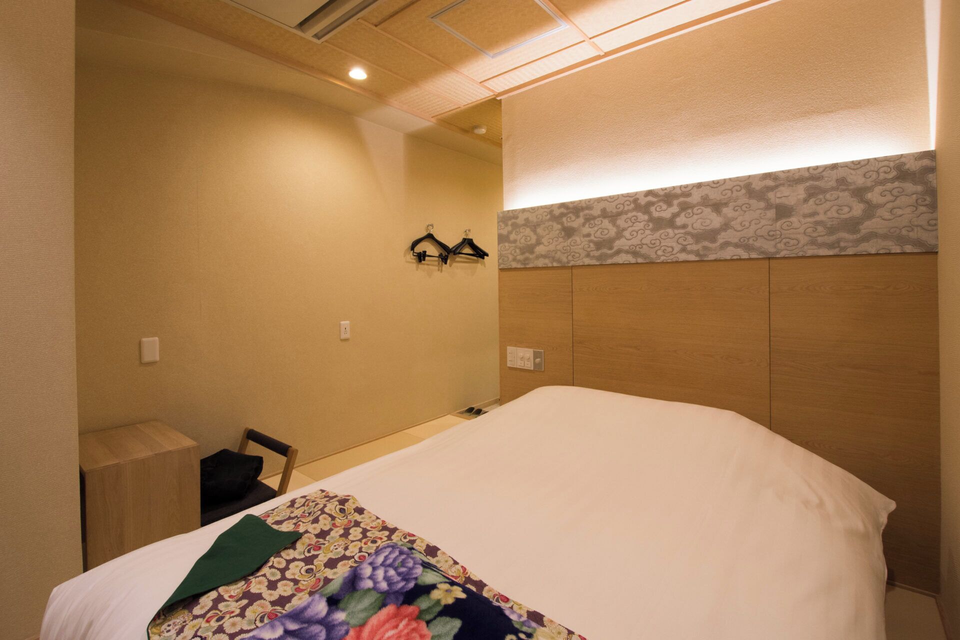 Habitación de hotel con una cama, una mesita de noche de madera, una silla y una lámpara de pared.