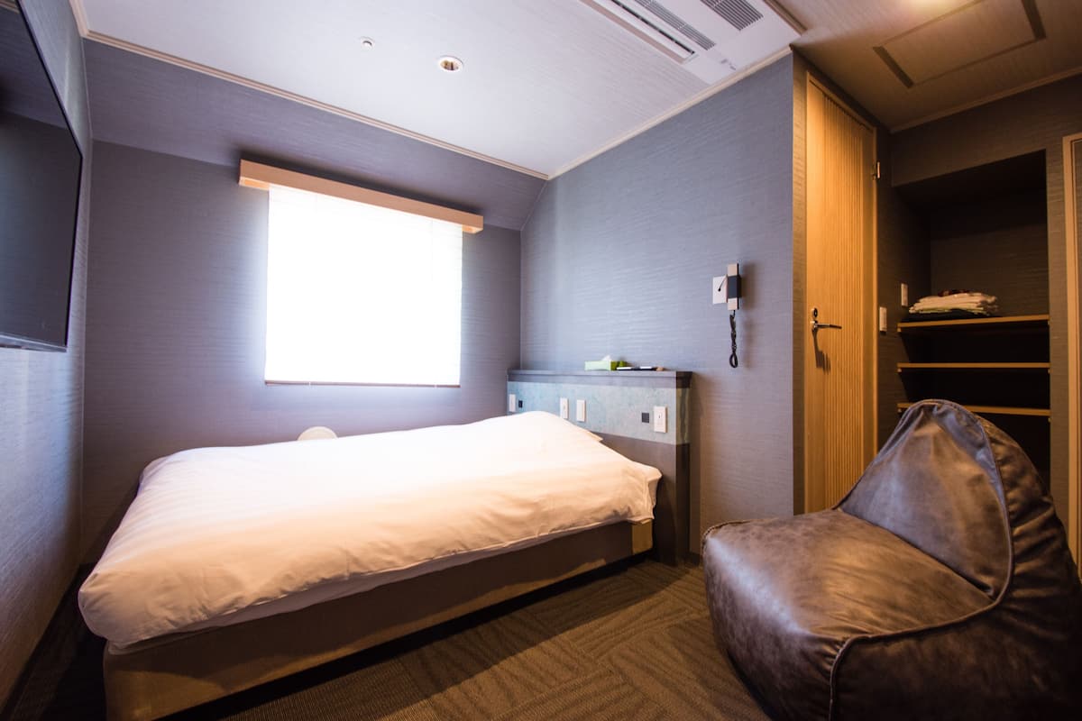 Habitación de hotel con una cama individual, una silla, un armario y una ventana.