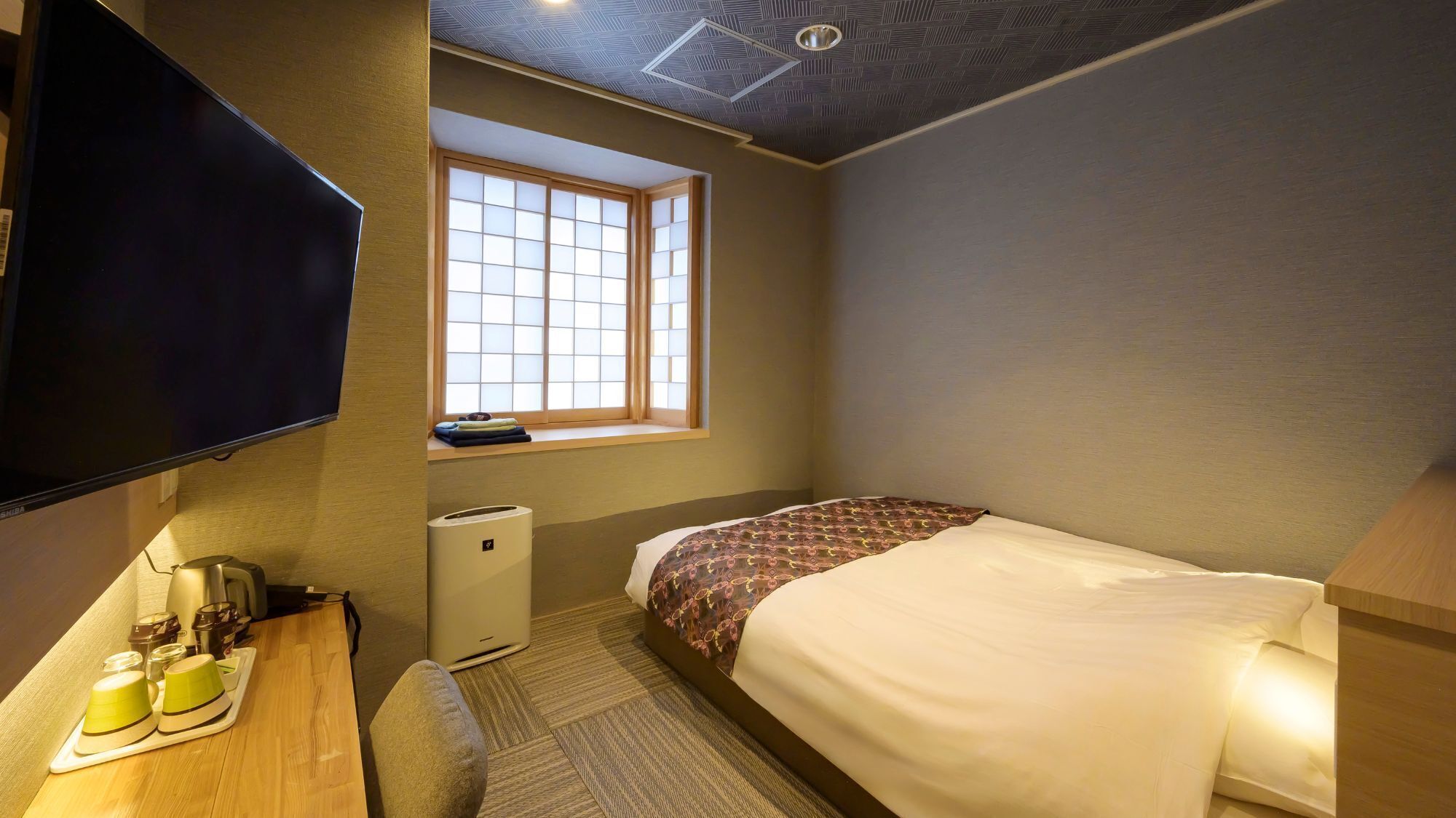 Ein Hotelzimmer mit Bett, Fernseher, Fenster, Schreibtisch mit Wasserkocher und einem kleinen Heizgerät.