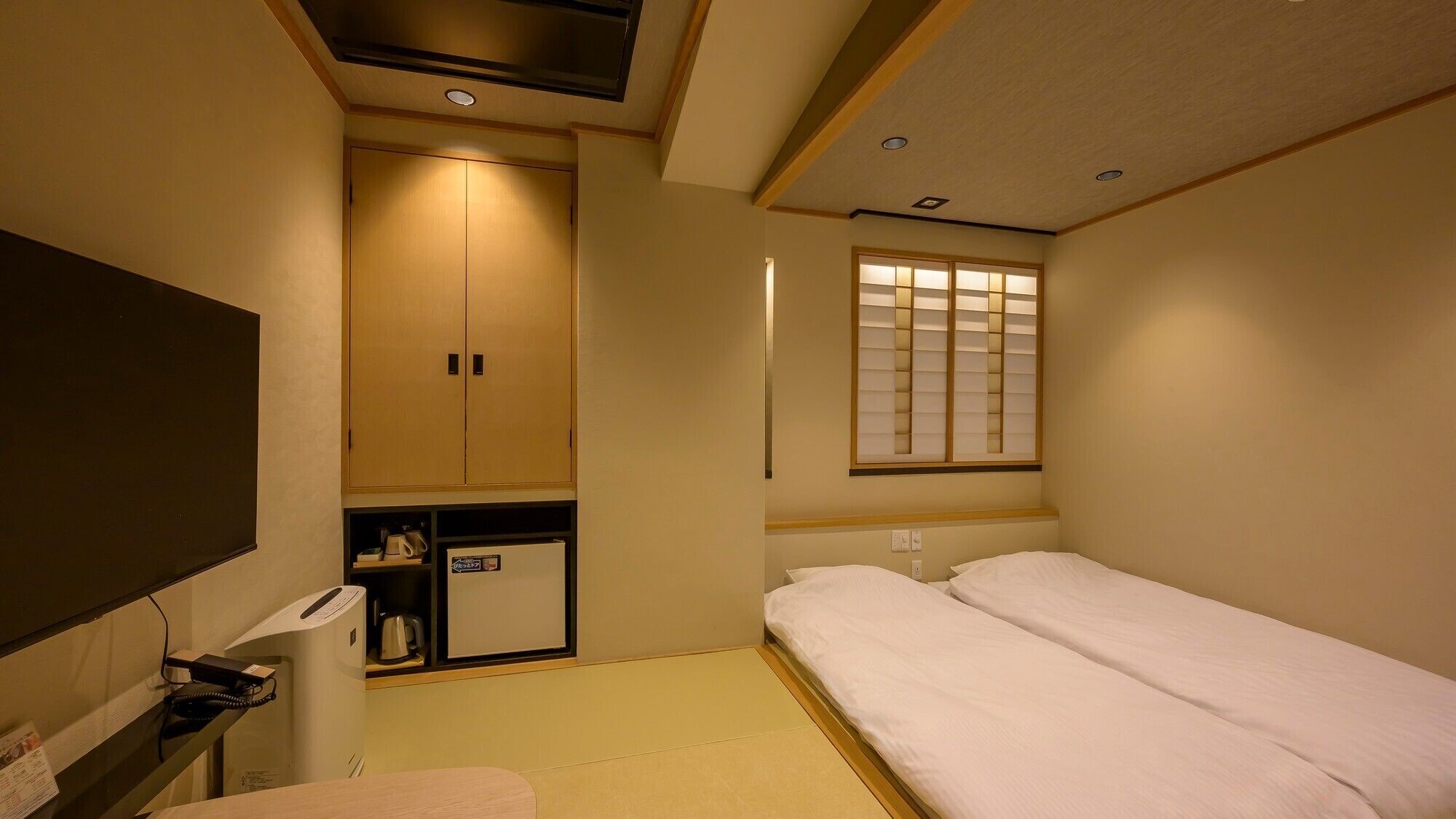Ein Hotelzimmer mit einem Bett, einem Schreibtisch mit Telefon, einem Schrank und einem Fenster mit Jalousien.