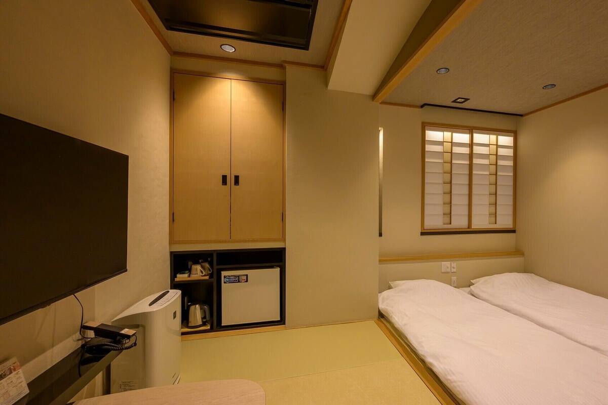 Una habitación de hotel con una cama, un escritorio con teléfono, un armario y una ventana con persianas.