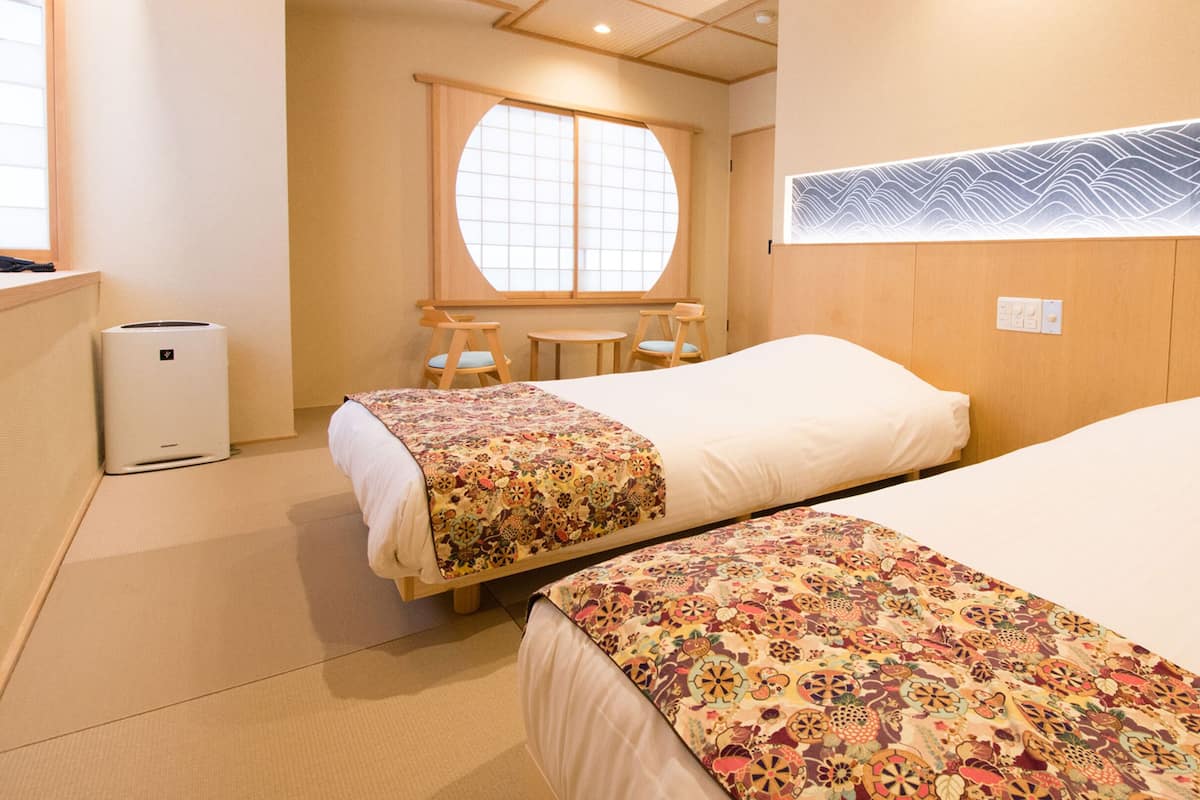 Habitación de hotel con dos camas, una mesita, una silla y una ventana con vistas al exterior.